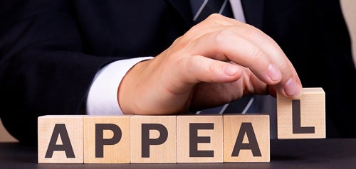 A man in a suit spelling the word APPEAL with wooden letter blocks
